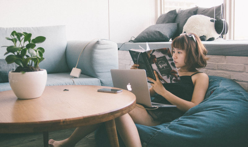 一个女人坐在白色的豆袋上，用MacBook在圆桌前放着绿叶植物|MacBook,书,人,休闲,可爱的,坐,女人,女商人,女孩,学习,室内,家具,工作,座位,房间,手机,技术,放松,木桌,枕头,桌子,椅子,植物,沙发,生活方式,电子,电脑,电话,移动,窗户,肉质,苹果,蓝色,设备,豆袋,阅读,风格-海量高质量免版权图片素材-设计师素材-摄影图片-mitapix-美塔图像