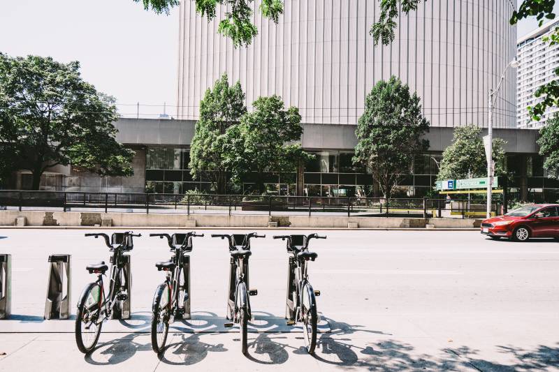 四辆停放在路边的黑色自行车|交通,人行道,商务,城市,城镇,夏季,市中心,建筑,户外,旅游,日光,树木,汽车,现代,白天,自行车,自行车停车场,车辆,运输系统,道路-海量高质量免版权图片素材-设计师素材-摄影图片-mitapix-美塔图像