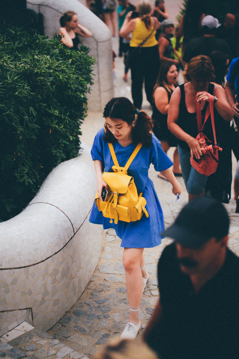 一个穿着蓝色衣服背着黄色背包的女人走近人群|人,人群,包,户外,散步,日光,穿着-海量高质量免版权图片素材-设计师素材-摄影图片-mitapix-美塔图像